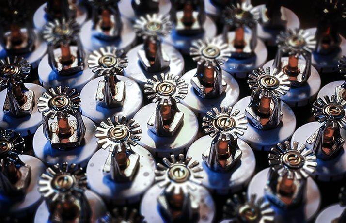 Rows of metal fire sprinkler heads with glass bulbs and circular escutcheons