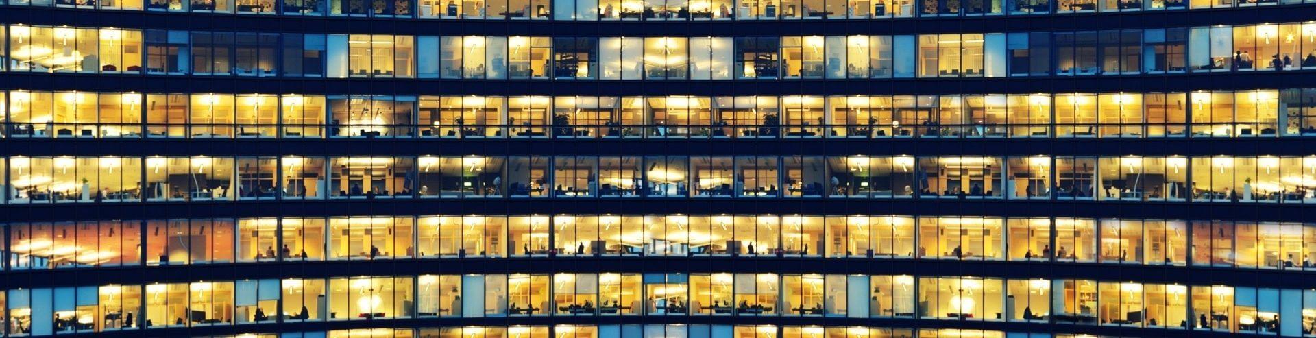 Illuminated office floors visible through a multistorey building’s windows at night